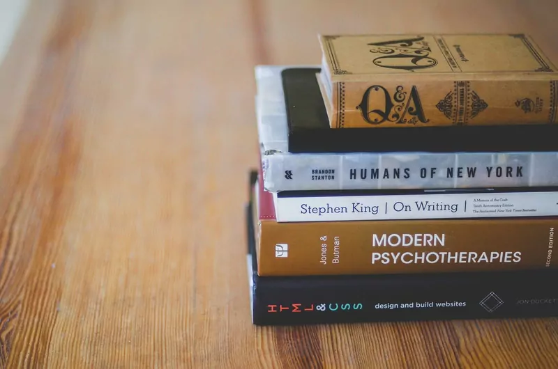 A small stack of nonfiction books lying on a wooden table, seen close up from the side