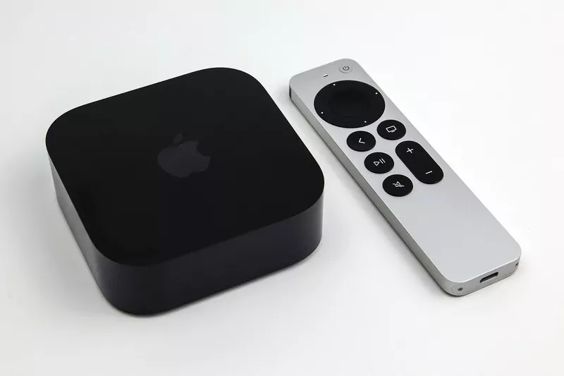 A black square Apple TV 4K box with an Apple logo beside a silver Siri Remote with a round touch pad, on a white surface