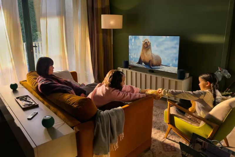 A family on a sofa watching a sea lion on a large TV, with two HomePod mini speakers on a table behind them and two more beside the TV