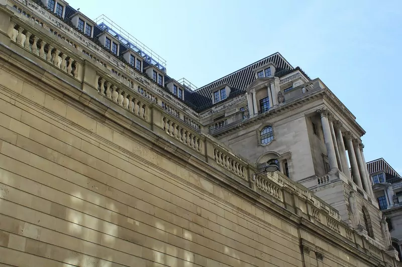 The high, windowless stone outer wall of the Bank of England, with the upper floors and dormer windows of the building rising behind it