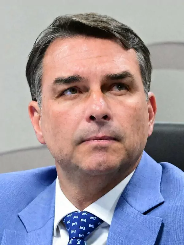 Flávio Bolsonaro, a dark-haired man in a light blue suit and blue tie, looking up