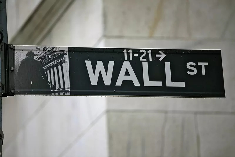 A black street sign reading Wall St in front of a stone building