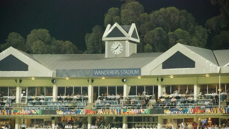 The pavilion at the Wanderers Stadium in Johannesburg at night, with a clock tower, the Wanderers Stadium sign, spectators on the balconies and colorful boards below