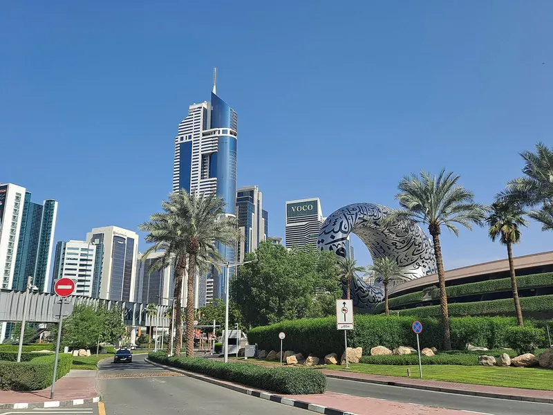 The silver ring-shaped Museum of the Future beside palm trees, a road and tall towers on a sunny day in Dubai