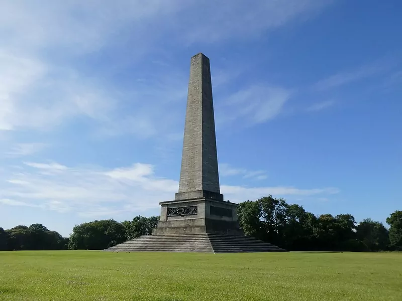The tall stone Wellington Monument obelisk standing on stepped base in a wide green lawn, with trees behind
