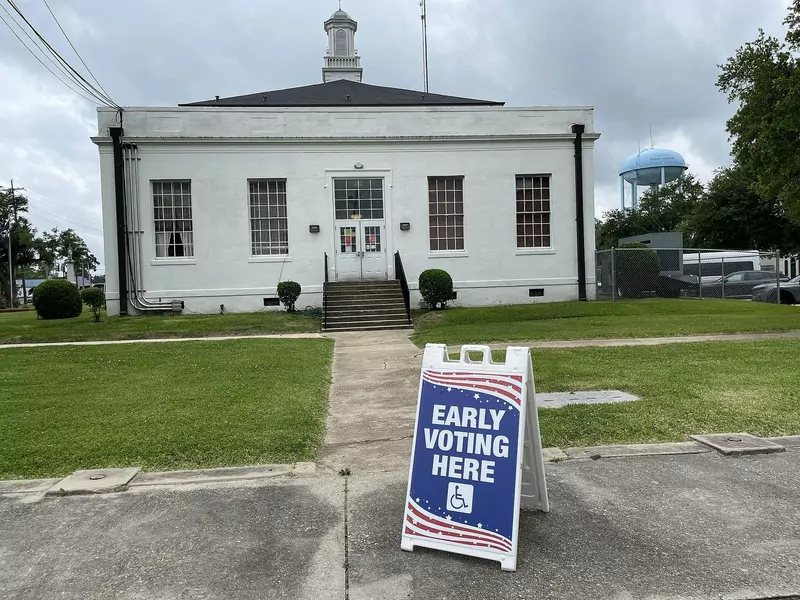 An Early Voting Here sign on the lawn in front of a white courthouse with columns under a cloudy sky