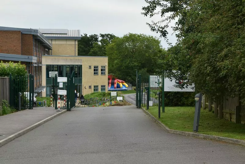 The driveway and gates leading to a modern school building surrounded by trees