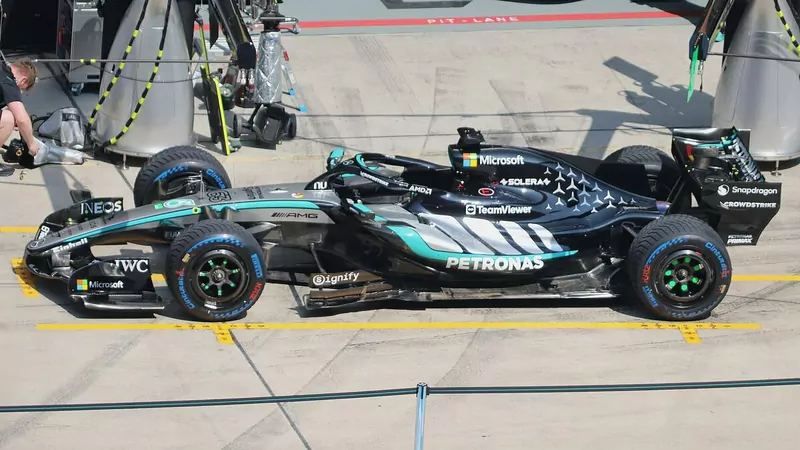 The black and teal Mercedes W17 Formula 1 car in a pit lane garage box, seen from the side