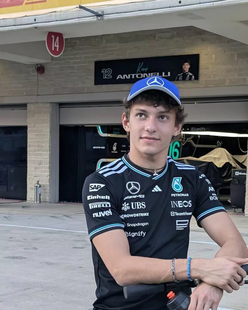 Kimi Antonelli in a black Mercedes team shirt and blue cap standing in front of his pit garage
