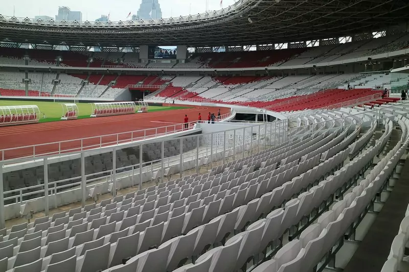 The red and white seats of Gelora Bung Karno Stadium in Jakarta, with the running track and dugouts beside the pitch