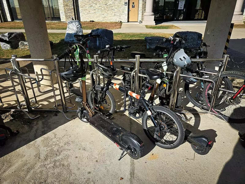 Electric scooters and bicycles parked together at a metal bike rack outside a building