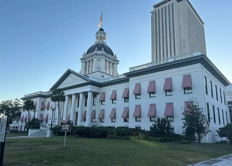 The white Old Florida Capitol with its dome and red and white striped awnings, with the tall modern Capitol tower behind it