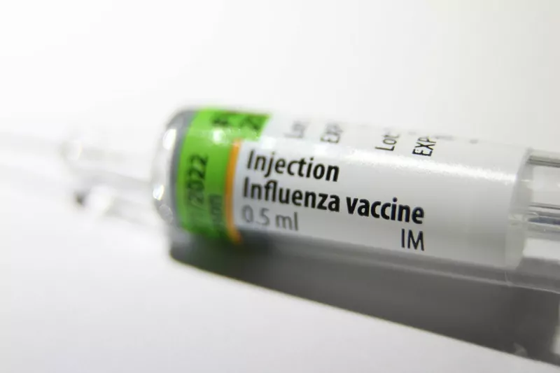 Close-up of a small glass ampoule labelled Injection Influenza vaccine 0.5 ml IM, lying on a white surface