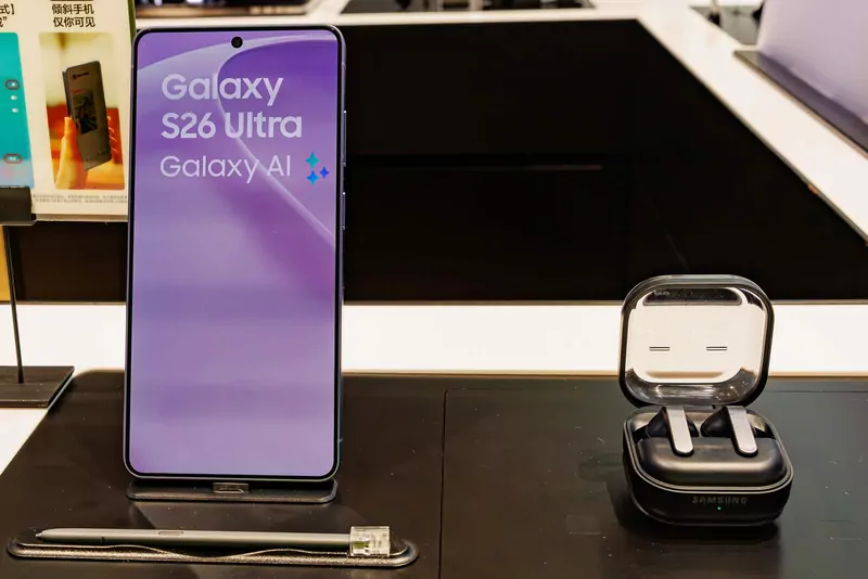 A Samsung Galaxy S26 Ultra standing on a display stand next to its S Pen and a pair of Galaxy Buds4 Pro earbuds in an open case