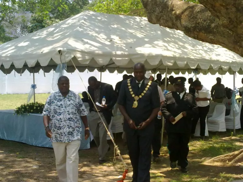 Officials in suits and printed shirts gathered around a handwashing station at an outdoor Global Handwashing Day event