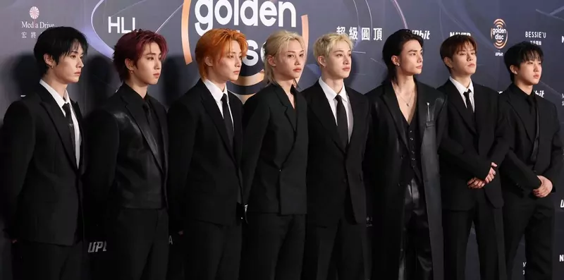 The eight members of Stray Kids in black suits on a red carpet in front of a Golden Disc Awards backdrop