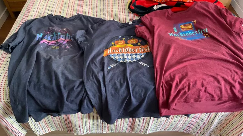 Three Hacktoberfest T-shirts from different years laid out on a bed