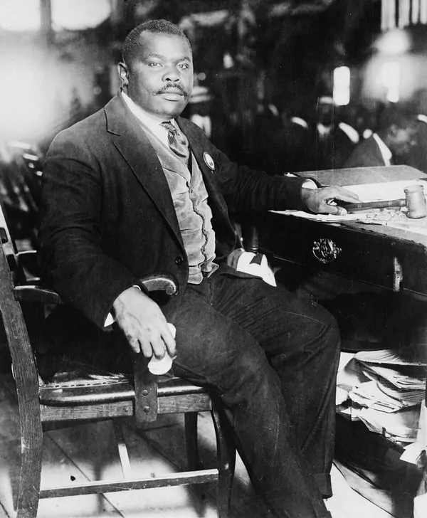 Black and white photo of Marcus Garvey in a suit and tie, seated at a desk with papers