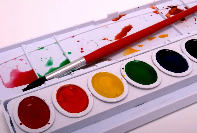 An open watercolour paint set with red, yellow, green and blue pans and a red paintbrush