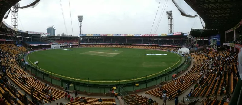 A wide view of M. Chinnaswamy Stadium in Bengaluru during a Test match, with yellow stands, a green outfield and floodlight towers