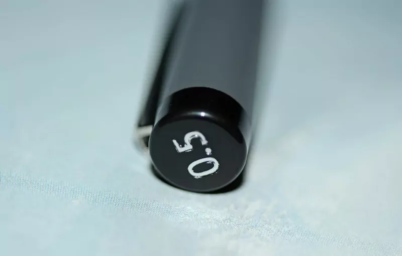 Close view of the black end cap of a fineliner pen marked 0.5 against a pale blue background
