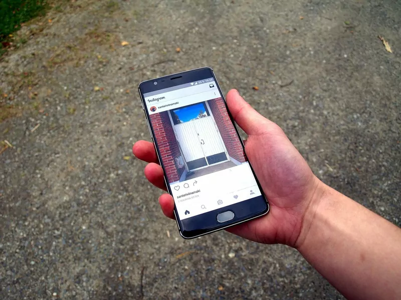 A hand holding an Android phone that shows the Instagram app with a photo of a white door in a brick wall