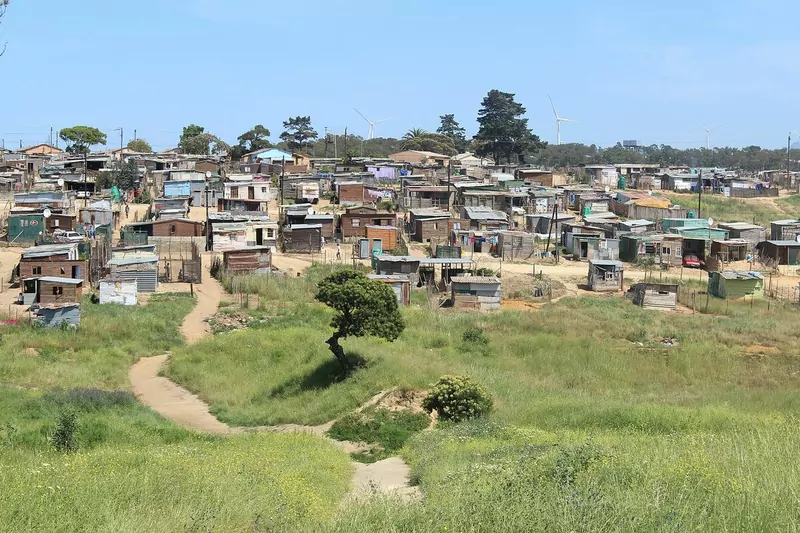 A large informal settlement of small houses on a green hillside near a rural town