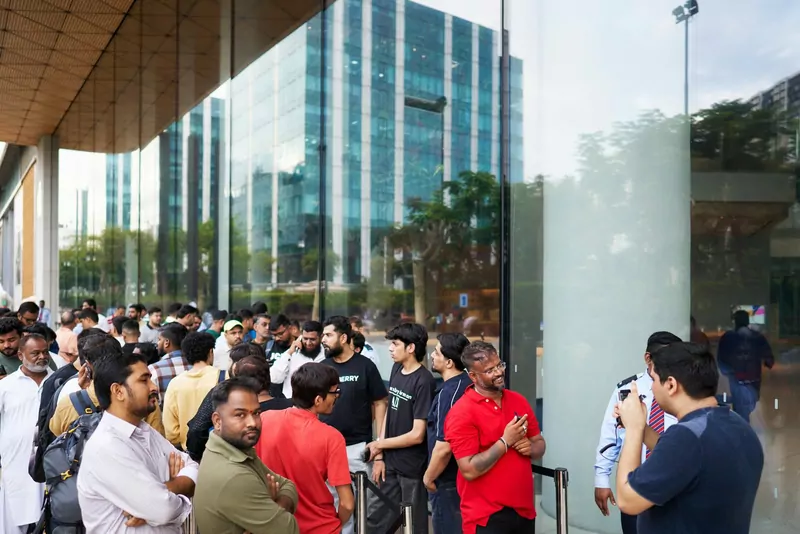 A crowd of customers waiting in line outside the glass front of the Apple BKC store in Mumbai
