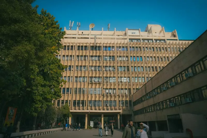 A wide view of IIT Delhi's main building with trees in front and students walking below