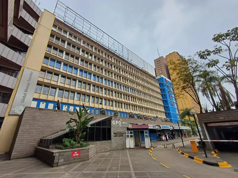 The General Post Office building in Nairobi: a cream and blue office block with rows of windows above a brick base, a paved plaza in front and a few trees on the right