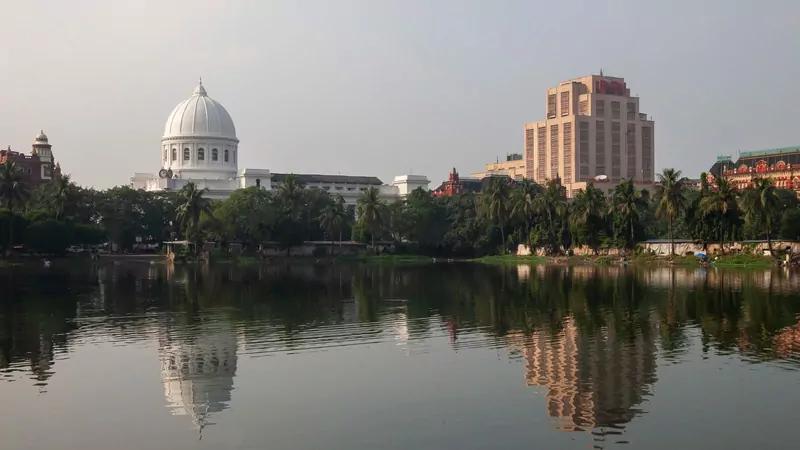 The white domed General Post Office and the tall Reserve Bank of India building in Kolkata, reflected in the still water of a pond