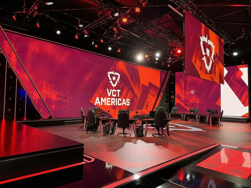 An empty esports stage with red lighting, player desks and large screens at the Riot Games Arena in Los Angeles