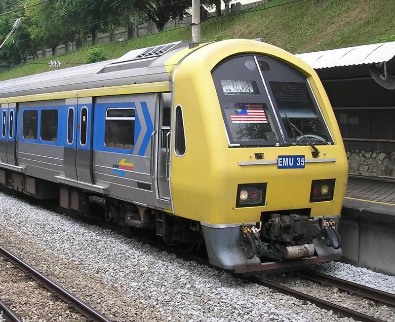 The yellow front of a blue and silver KTM Komuter electric train, numbered EMU 35, stopped at a platform beside a grassy bank