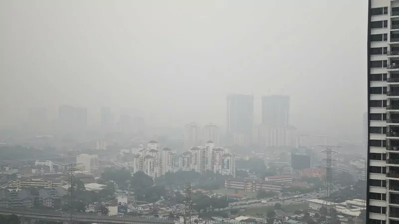 A thick grey haze over Kuala Lumpur, with apartment blocks, a road and an elevated rail line fading into the smog and a tall residential tower at the right edge