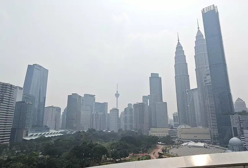 The Petronas Towers and the Kuala Lumpur skyline dimmed by haze, seen over the trees of KLCC Park