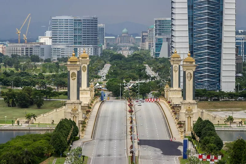 The Seri Gemilang Bridge in Putrajaya with its gold-topped cream pillars, a wide empty road and the green-domed Perdana Putra office complex far down the avenue