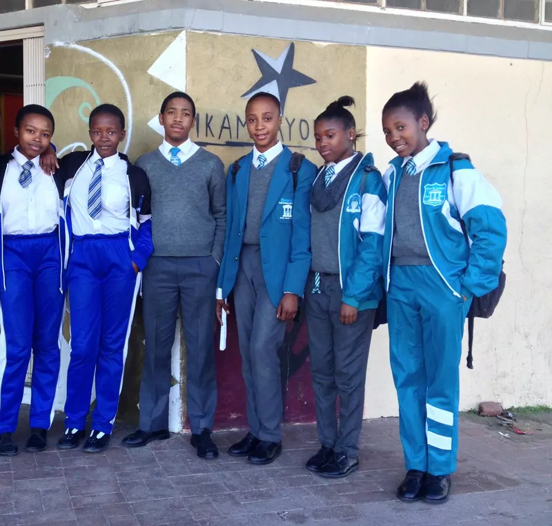 Five learners in school uniform, blazers, ties and tracksuit trousers, stand in a row outside their school in Khayelitsha, Cape Town