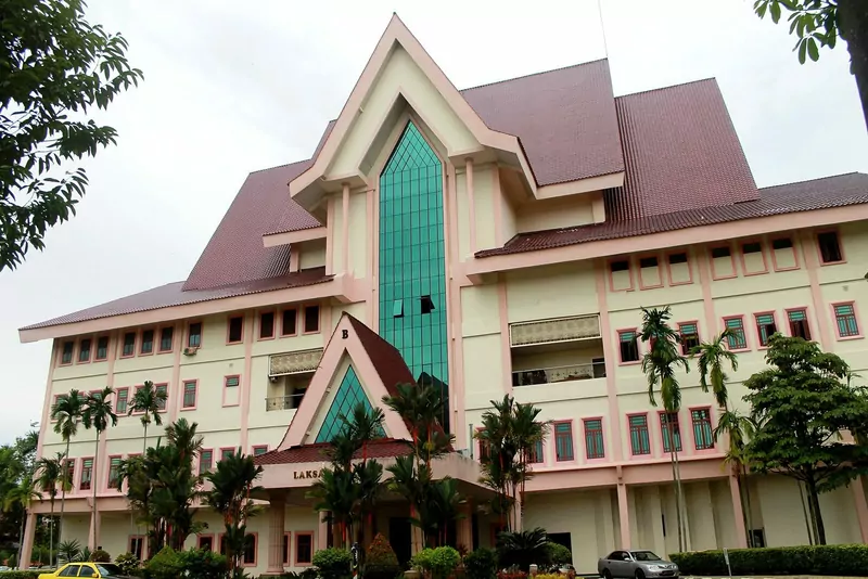 The five-storey cream Blok Laksamana building at Seri Negeri with a steep brown tiled roof, pink trim, a tall green glass panel in the middle and palm trees in front