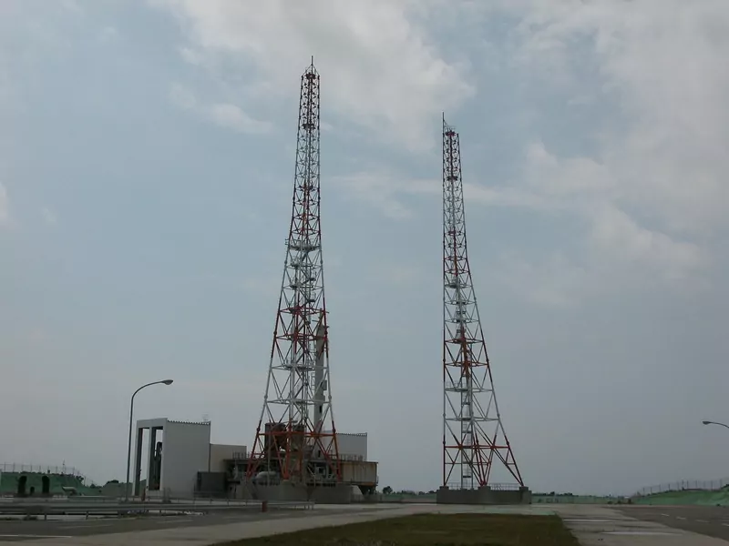 Two tall red and white steel towers at a rocket launch pad under a cloudy sky