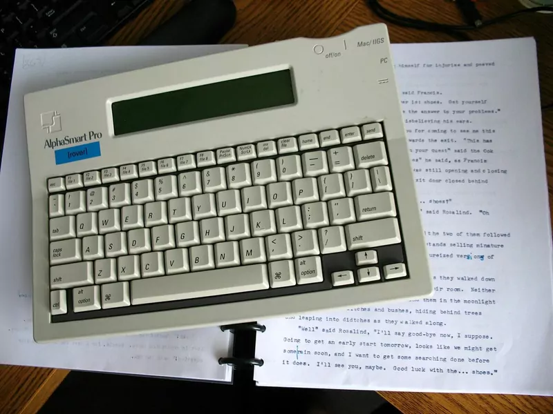 An old AlphaSmart portable keyboard lying on printed pages of a novel draft