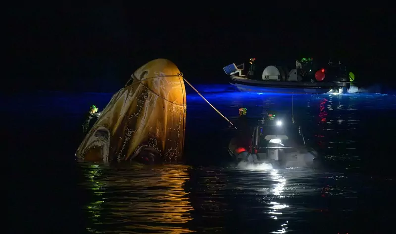 Recovery teams in small boats work around a scorched SpaceX Dragon capsule floating in the dark Pacific Ocean at night