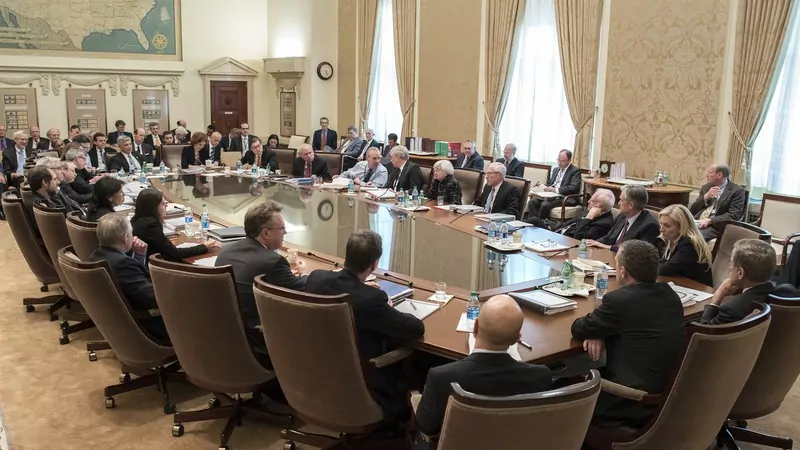 Federal Reserve officials seated around a long oval table in a wood-panelled boardroom with tall windows