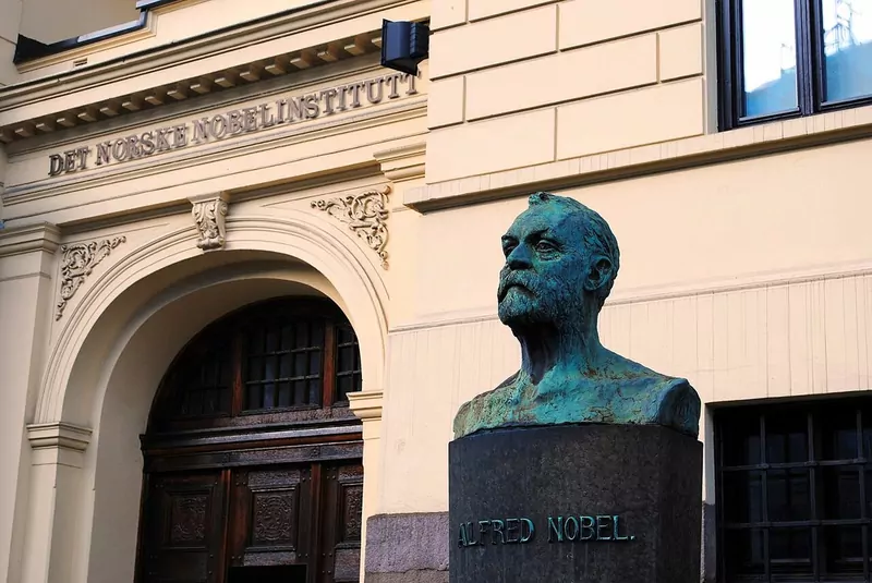 A green bronze bust of Alfred Nobel in front of the arched doorway of the Norwegian Nobel Institute building