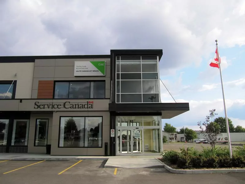 A modern two-storey office building with a Service Canada sign and a Canadian flag on a pole beside the entrance