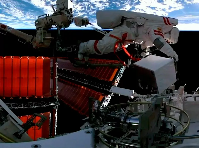 A Chinese astronaut in a white spacesuit working outside the Tiangong space station with Earth in the background
