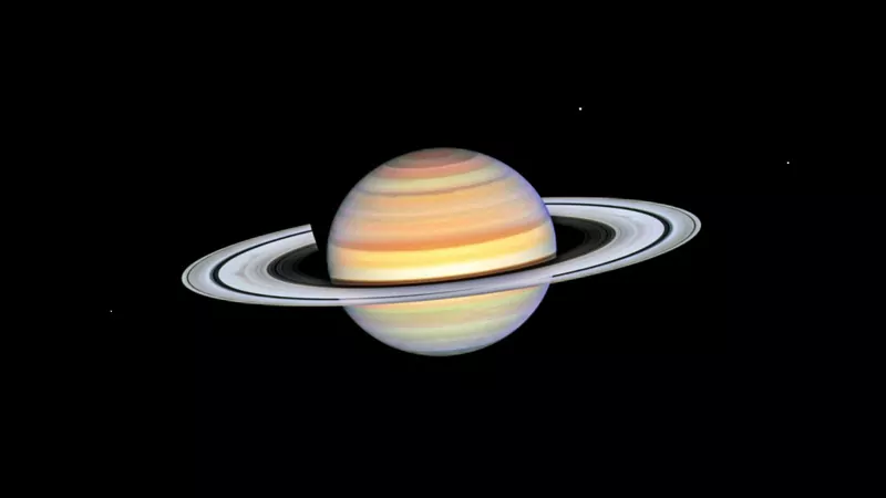 Saturn with pale bands of cream, orange and pink and a ring system with a dark gap, on a black background
