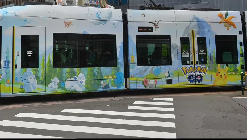 A tram painted with Pokémon characters and the Pokémon GO logo crosses a city street
