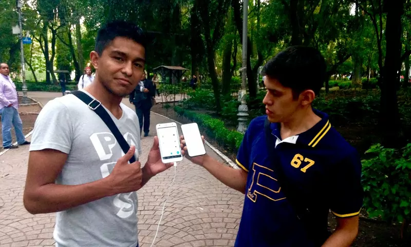 Two young men in a park hold up their phones to compare the game on their screens