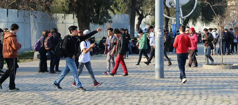 A crowd of young people walking and looking at their phones on a cobbled park square
