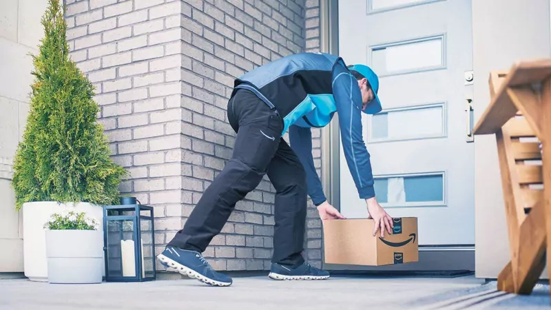 An Amazon delivery driver in a blue uniform placing a box with the Amazon smile logo at the front door of a house